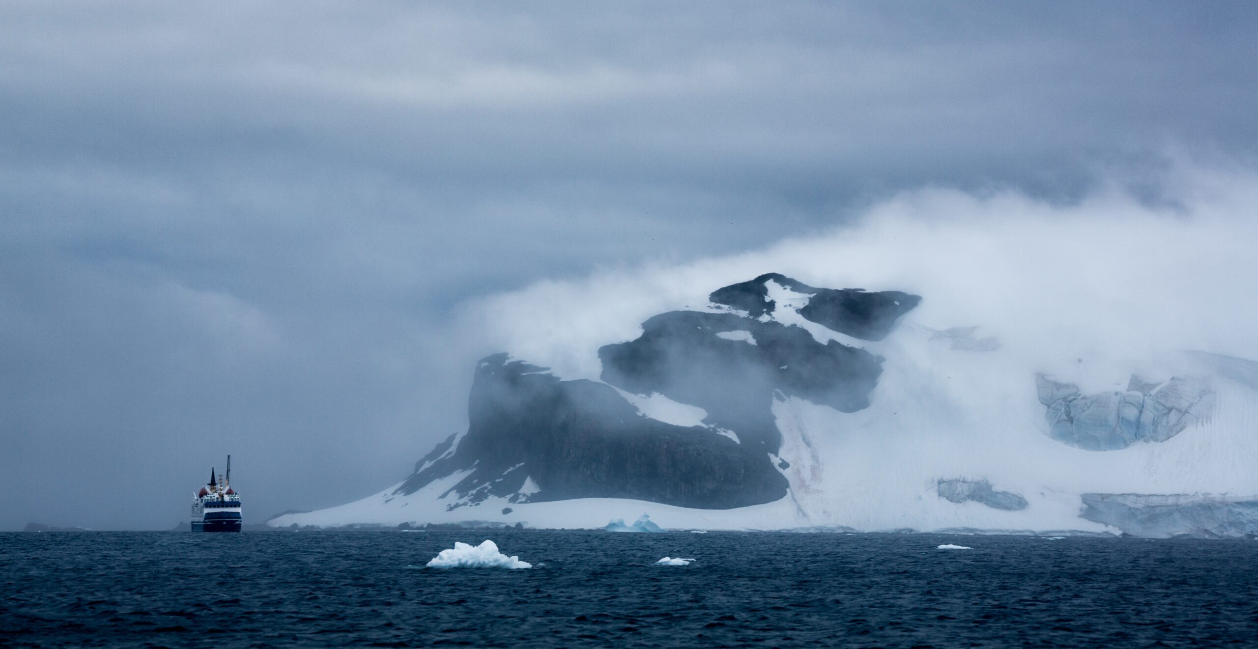 An aerial shot of a ship and iceberg in Antarctica under cloudy sky