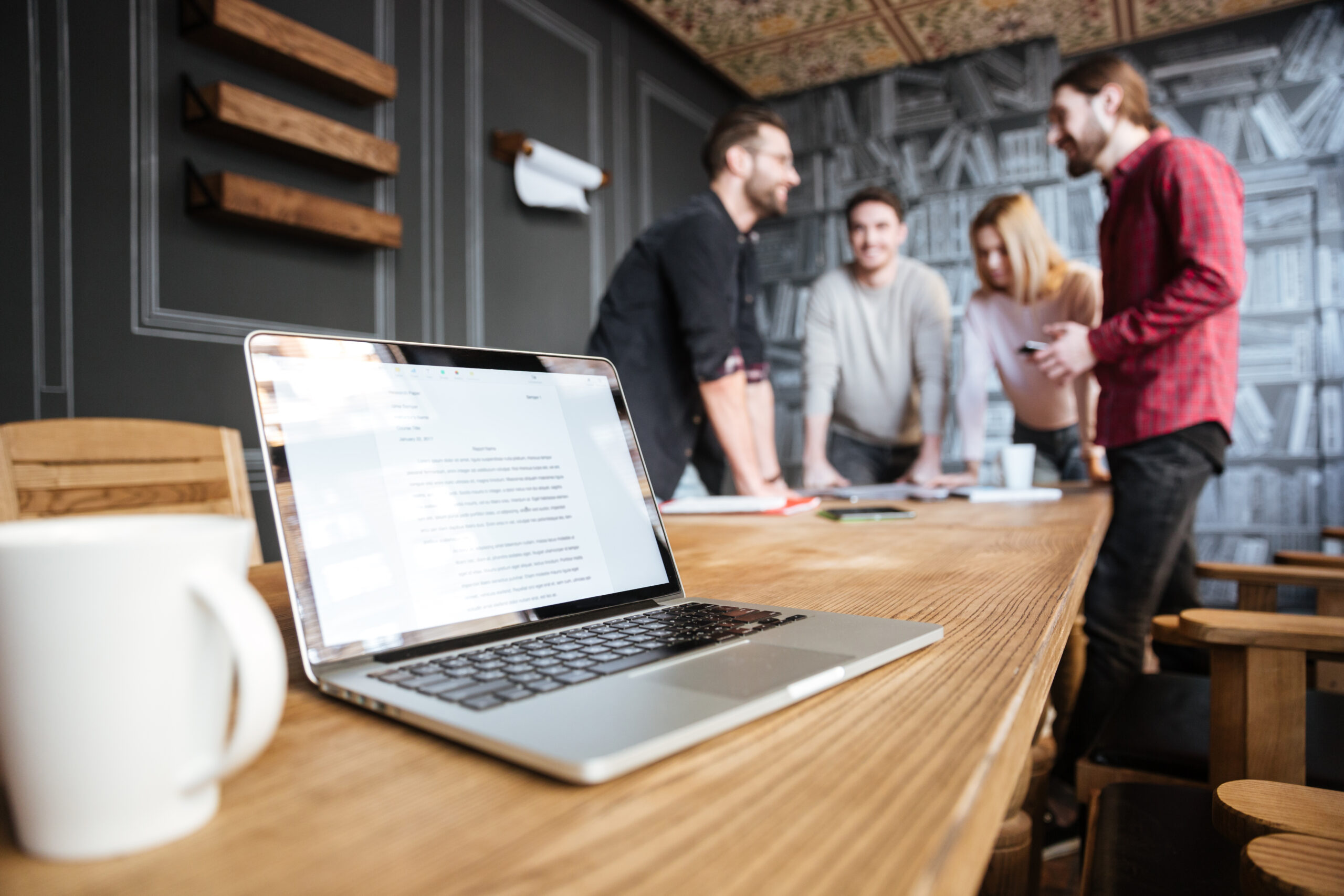 Image of young attractive colleagues standing in office and coworking. Focus on laptop.