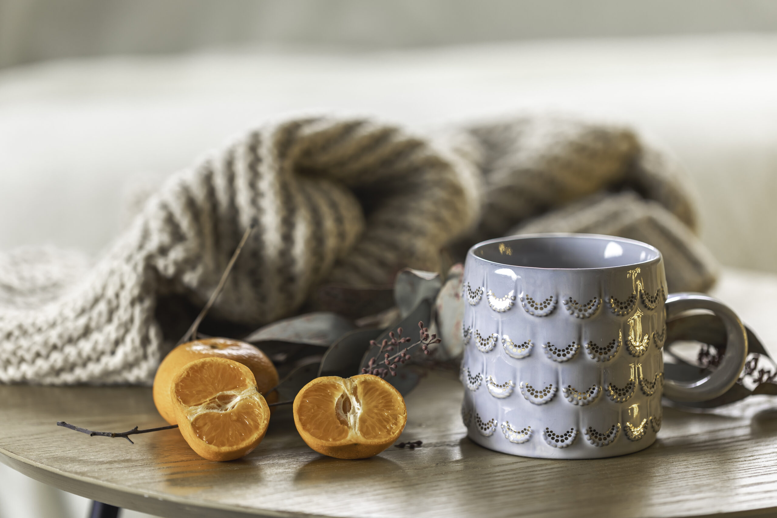 Close-up, shiny gray cup and tangerines on a blurred background with a knitted element. Copy space.